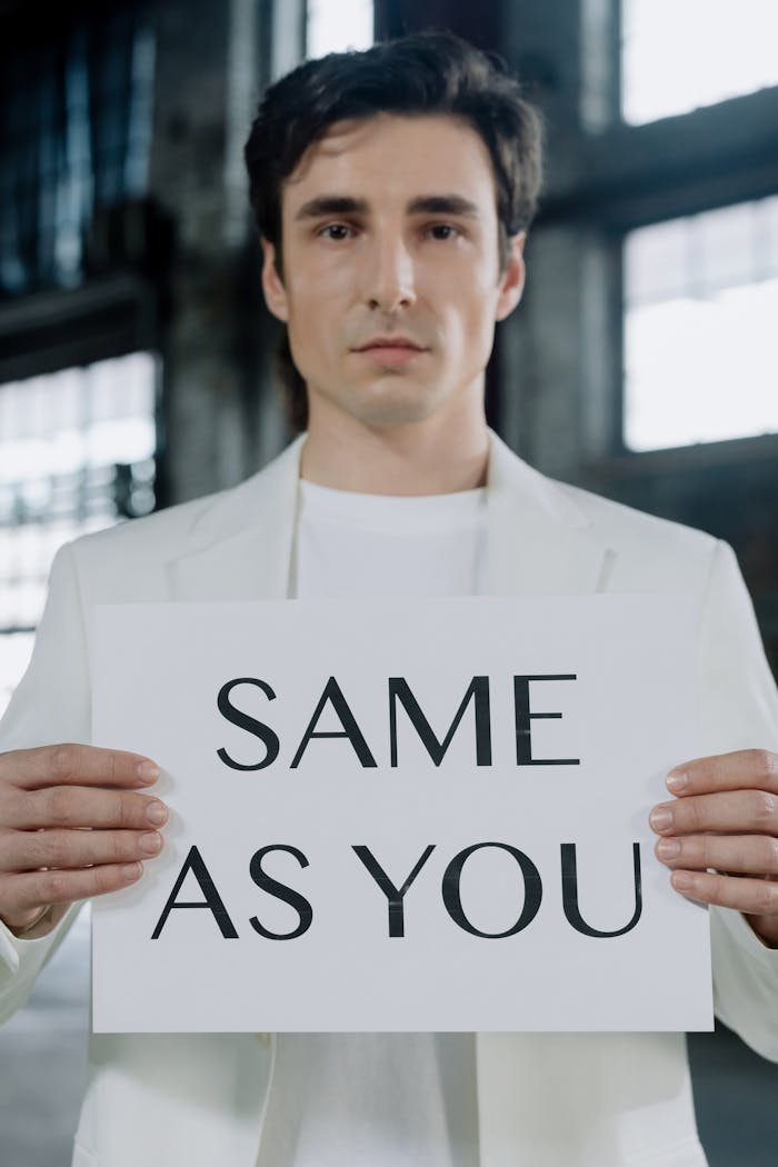 A man in a white suit holds a sign reading 'Same As You,' promoting equality.