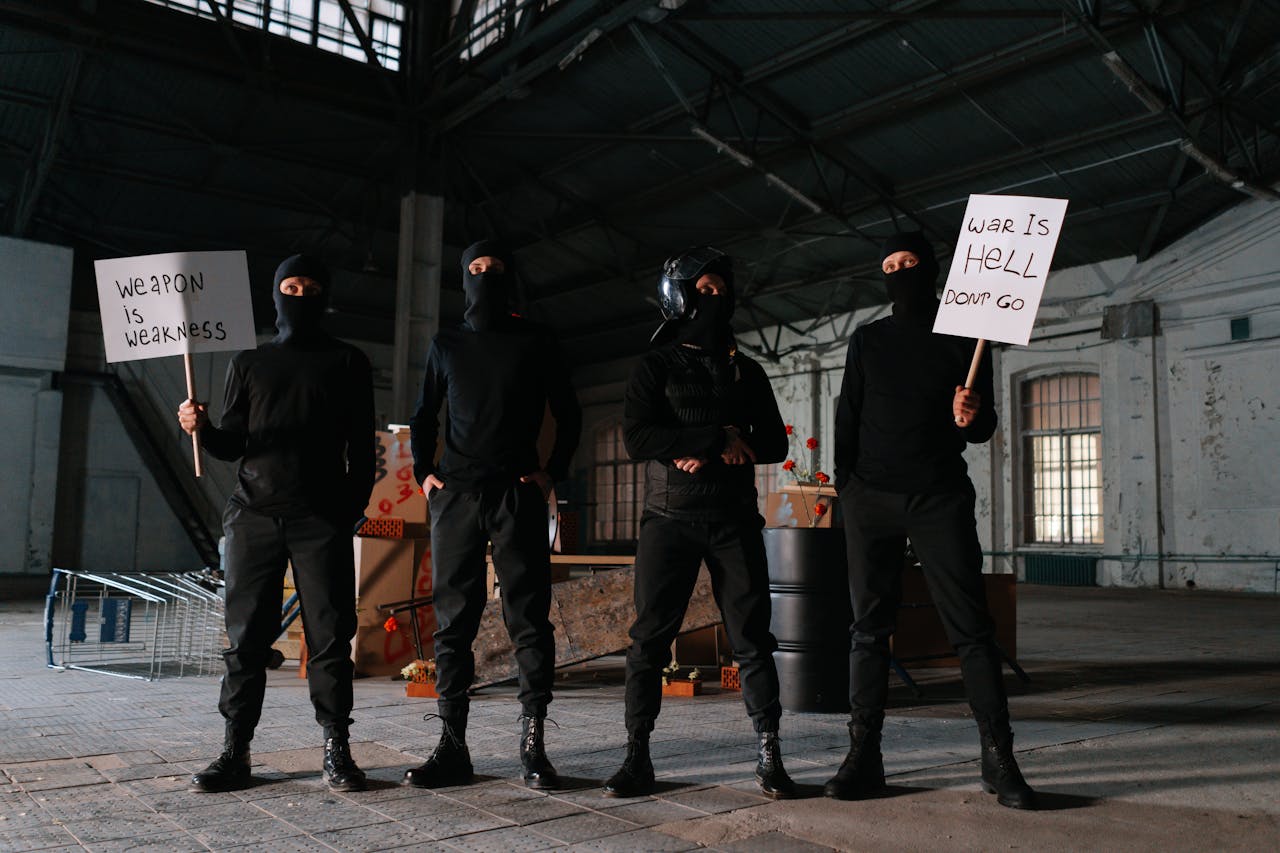 Four masked protesters stand indoors with anti-war signs, advocating peace.