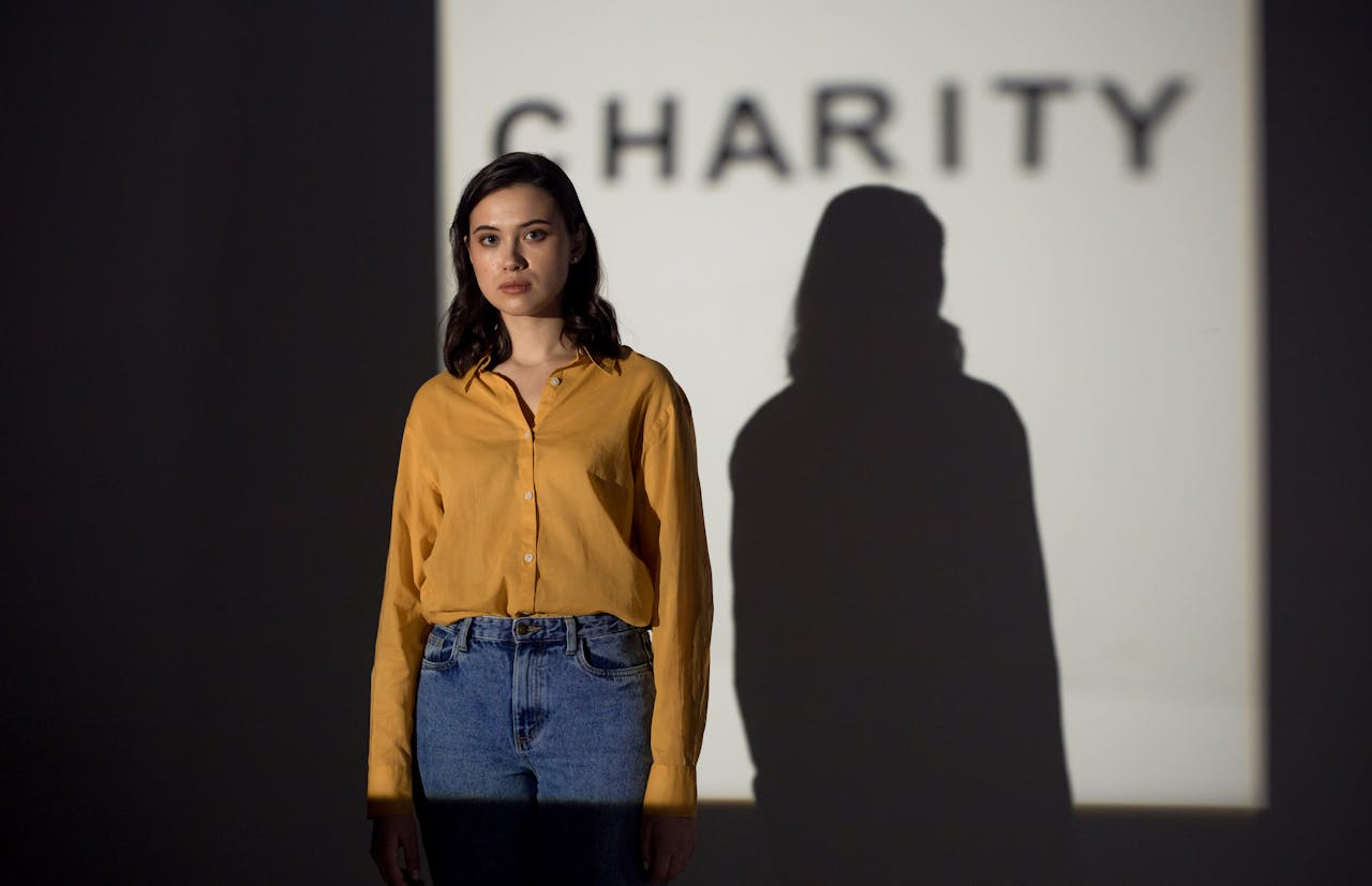 Asian woman in orange shirt, shadow cast against charity sign, indoors.